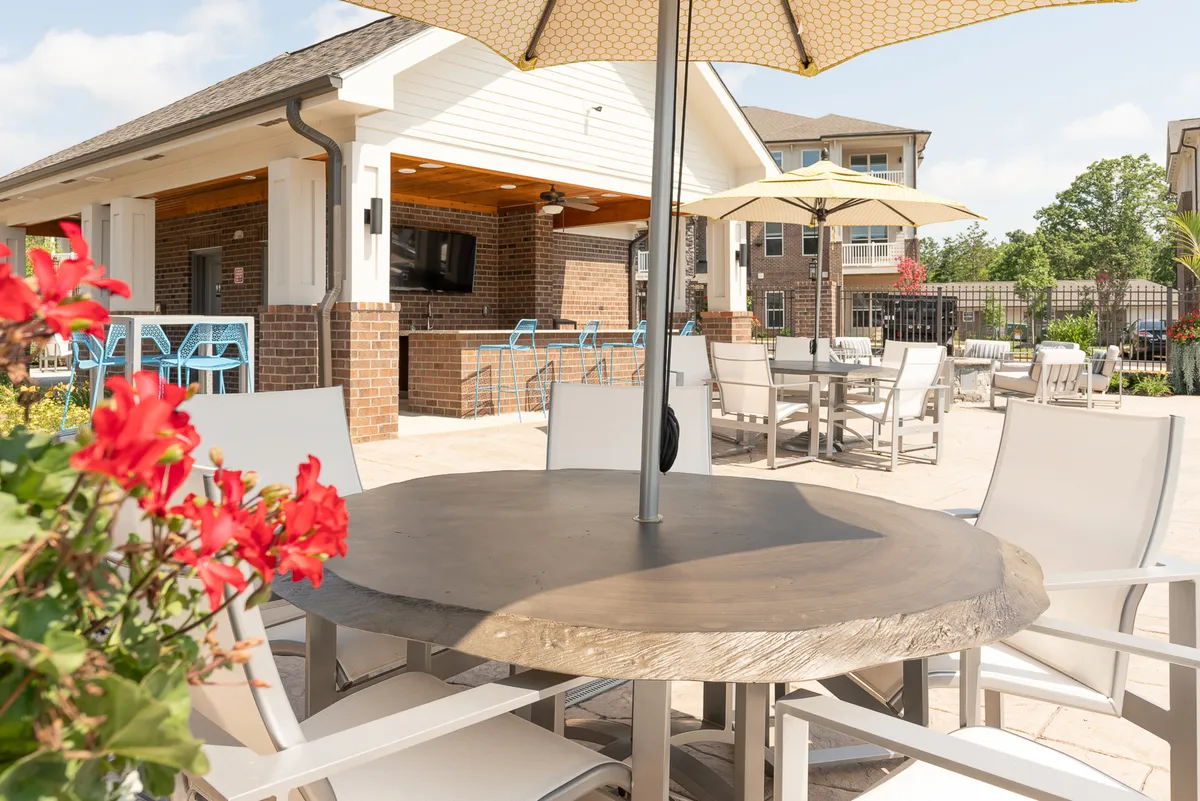 An exterior patio scene with a well-appointed outdoor dining table, umbrellas, and a bar area. The setup is ideal for socializing, dining al fresco, or informal networking events, set against a backdrop of cheerful ambiance.
