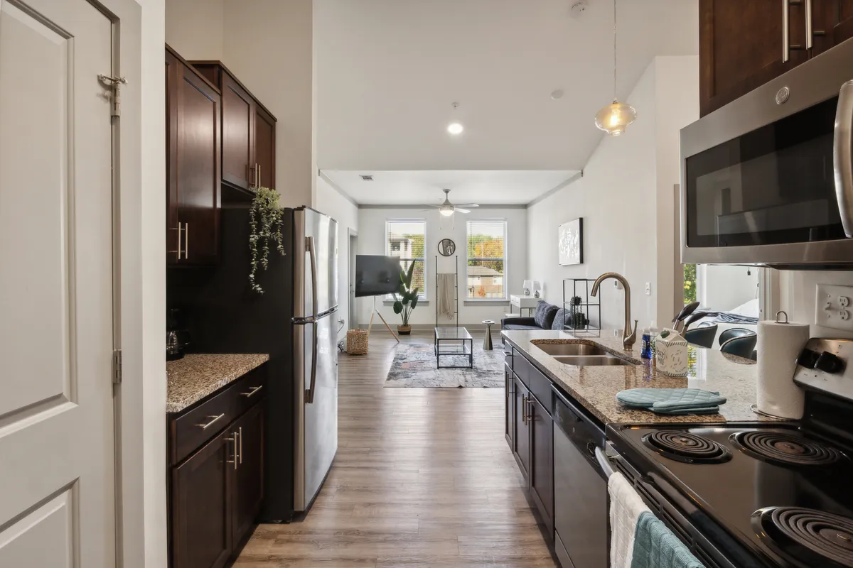 A spacious interior with granite countertops, modern appliances, and an open layout. Large windows bathe the room in natural light, enhancing the welcoming mood. The visible space hints at both living and dining areas, emphasizing functionality and style.