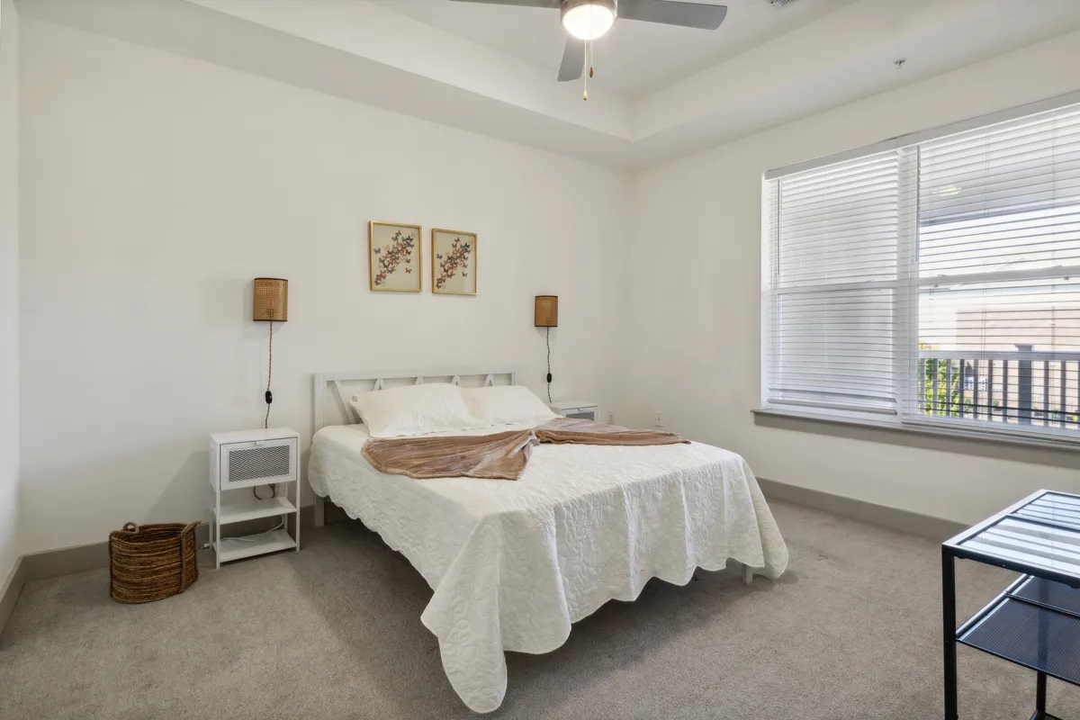 A serene bedroom scene featuring a neatly made bed with crisp white bedding, flanked by two nightstands with softly glowing lamps. Above the headboard, tasteful artwork adds a personal touch, while the tranquil mood invites relaxation and restful sleep.