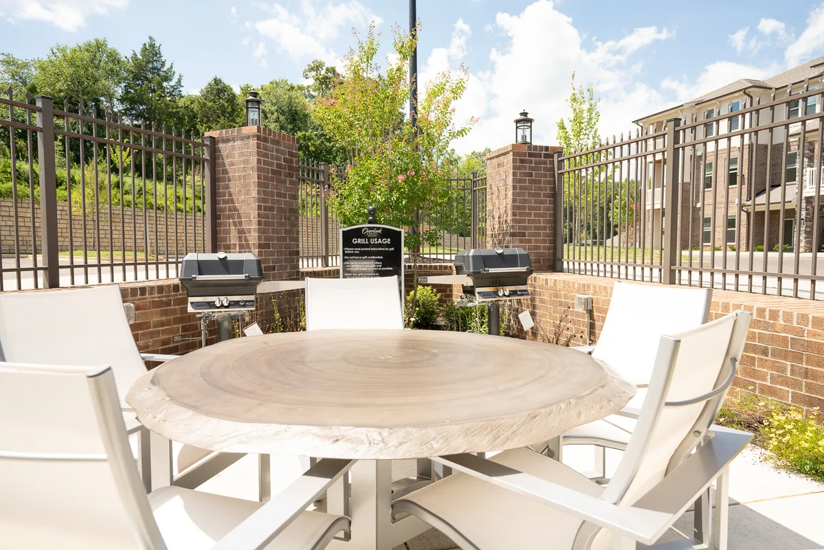 Surrounded by lush greenery, this exterior image features a wooden table and built-in grill stations, creating a relaxed space for outdoor dining, barbecues, and social gatherings. The setting feels both tranquil and communal.