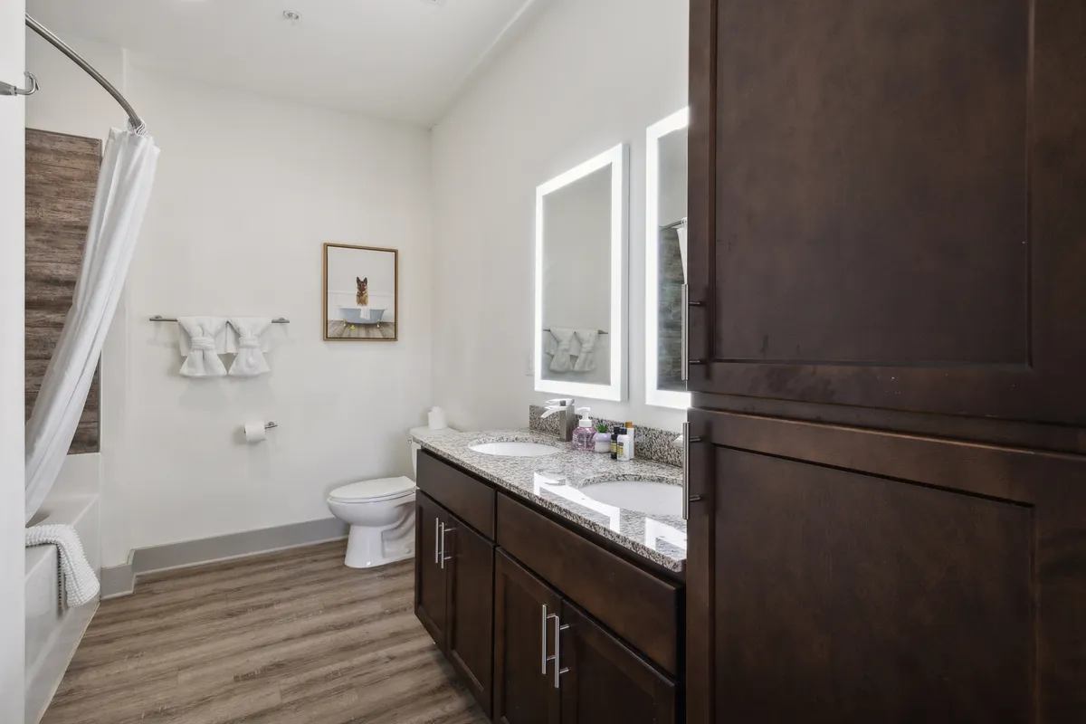 A serene bathroom with a granite countertop, dual mirrors, wooden cabinetry, and decorative wall art. The inviting atmosphere is perfect for calming baths or invigorating morning routines.